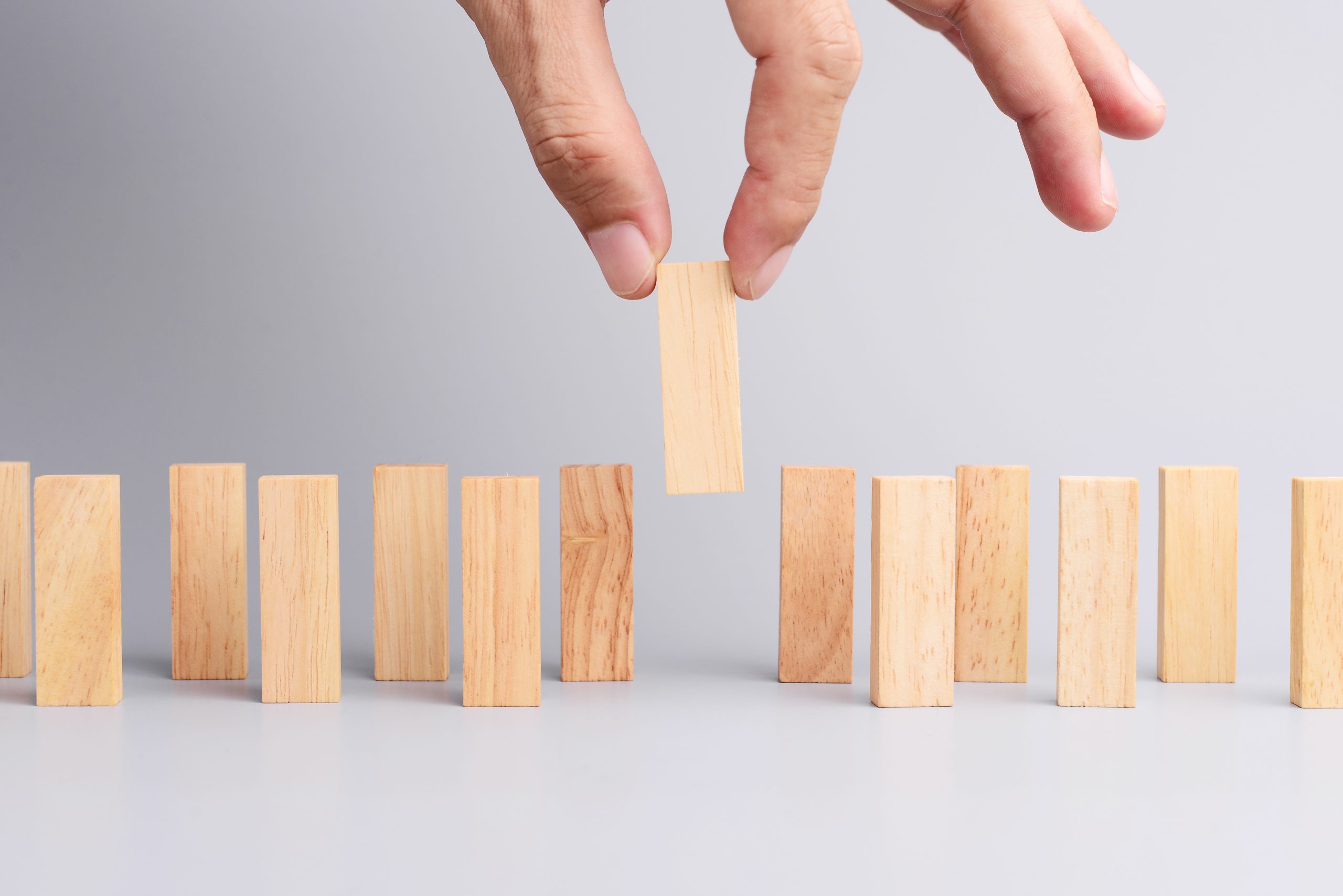 Man hand pick one of wood block from many wood block in row, metaphor to business concept in choose ideal person from many candidate. Gray background, side view.